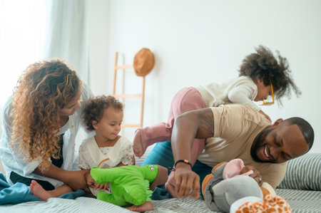 Happy African American Parents with  little daughters playing on the bed in bedroom at home, happy...