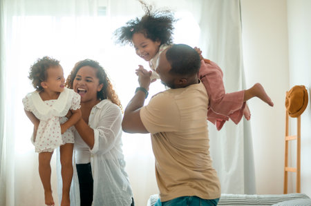 Happy African American Parents with  little daughters playing on the bed in bedroom at home, happy...