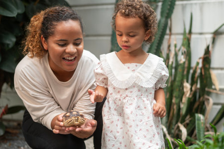 African American mother holding turtle on  her hand showing to a  girl in gardenの写真素材