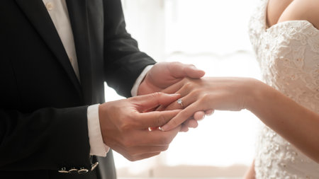 Close up of Groom putting diamond engagement ring on bride's finger in wedding ceremony