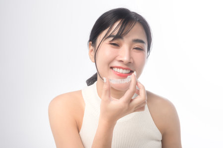 Young smiling woman holding invisalign braces over white background studio, dental healthcare and Orthodontic concept.の写真素材