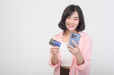 Asian smiling woman holding credit card over white background studio, shopping and finance concept.の写真素材