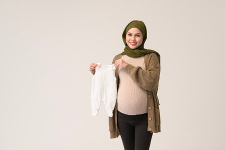 Portrait of Pregnant muslim woman in hijab holding baby cloth over white background studioの写真素材