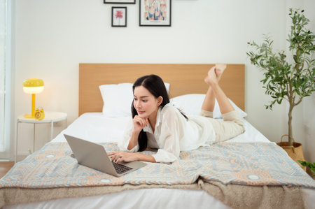 Young Asian woman enjoying using laptop computer in bedroom at home