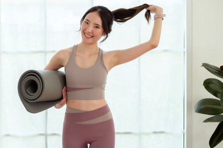 Young Asian woman wearing yoga holding mat in studio