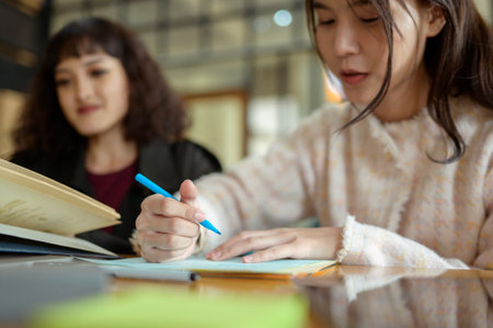 Two friends collaborate on schoolwork at a cozy cafe table, sharing ideas and materials.の写真素材