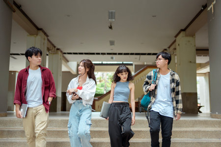 Four students walk together on campus, chatting and carrying their books and supplies.の写真素材