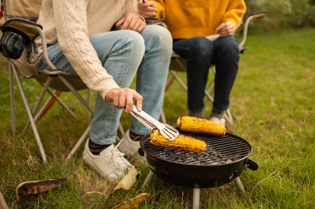 Friends grill skewers and corn while relaxing in a backyard on a warm afternoon.の写真素材