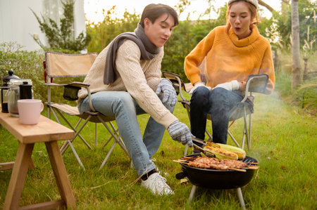 Couple Grilling food on a portable barbeque while relaxing in a garden on a warm afternoon.の写真素材