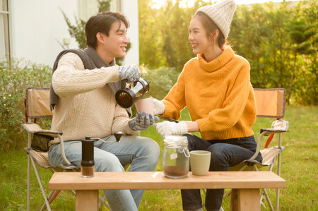 Two friends relax in a garden, sipping warm drinks and engaging in conversation on a sunny day.の写真素材