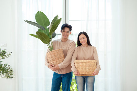 A couple joyfully holds indoor plants and wicker baskets in a bright, airy living space.の写真素材