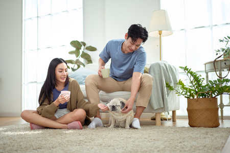 A couple relaxes on the floor with their pug, sharing a light breakfast in a sunny room.の写真素材