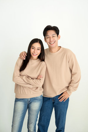 A young couple poses with smiles, dressed in beige tops and denim jeans, exuding happiness.の写真素材