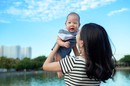 A mother enjoys a playful moment with her baby by the serene lake under a bright sky.の写真素材