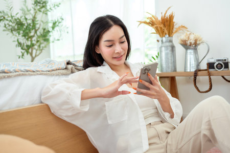 Young asian woman using smart phone lying on bedの写真素材
