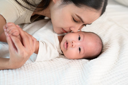 A mother shares a tender moment with her baby, showing affection on a soft bed.の写真素材