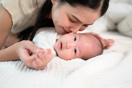 A mother shares a tender moment with her baby, showing affection on a soft bed.