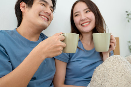 Two people laugh and sip coffee while sitting on a bedroom floor filled with morning light.の写真素材
