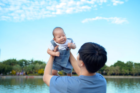 A father is playfully lifting his smiling baby above him in a park on a clear day.の写真素材