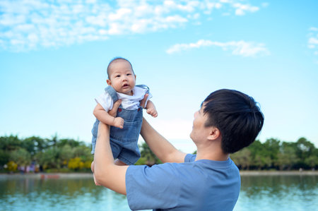 A father is playfully lifting his smiling baby above him in a park on a clear day.の写真素材