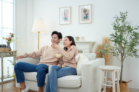 Two people share laughter while sitting on a comfortable couch in a stylish living room.の写真素材