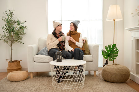 A couple sits comfortably on a sofa, each holding a cup and smiling happily together.の写真素材