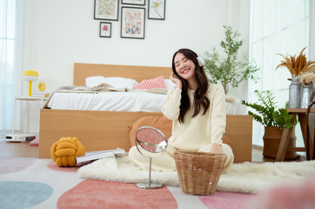 Young Asian woman wearing headphones enjoying music in bedroom at home