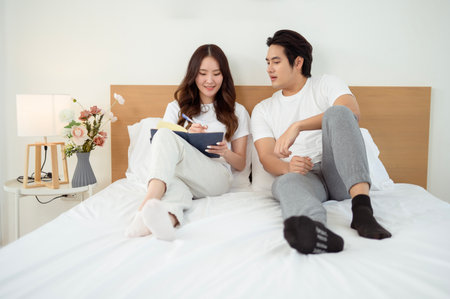 A couple brainstorms ideas on a bed as one writes in a notebook.の写真素材