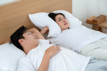Man is snoring while woman is trying to sleep beside him in a cozy bedroom.の写真素材