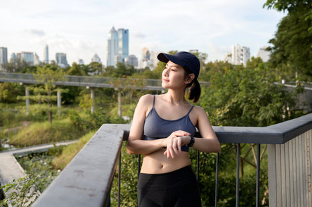 A woman in athletic wear monitors her smartwatch in a green urban park during daylight.の写真素材