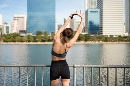 Fitness enthusiast stretches by a city waterfront, enjoying a bright and sunny day.の写真素材