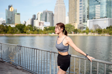 A woman stands by a lake in a city, embracing the warm sun as she enjoys outdoor fitness.の写真素材