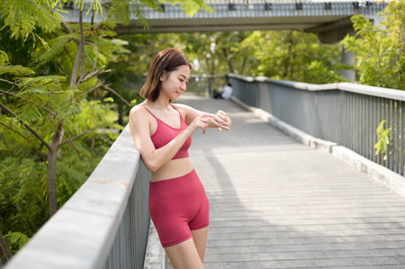 Woman in activewear monitors her fitness tracker during a workout in a lush park.の写真素材