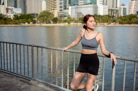 A woman stands by a lake in a city, embracing the warm sun as she enjoys outdoor fitness.の写真素材