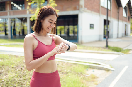 Woman checks her fitness watch while jogging in a lively urban environment during daytime.の写真素材