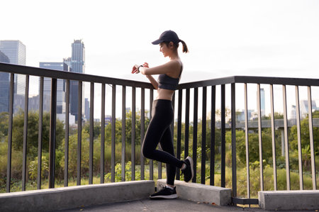 A woman in athletic wear monitors her smartwatch in a green urban park during daylight.の写真素材
