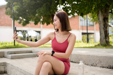 A woman sits on a concrete bench smiling while browsing her smartphone.の写真素材