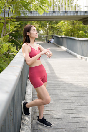 Woman in activewear monitors her fitness tracker during a workout in a lush park.