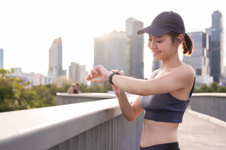 A woman in athletic wear monitors her smartwatch in a green urban park during daylight.の写真素材