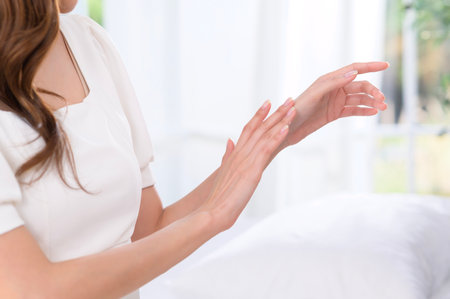 A woman enjoys applying a cream to her hand with a joyful expression in a well-lit setting.の写真素材