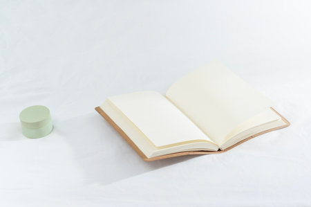 An open notebook on a light surface with a green container invites creativity.