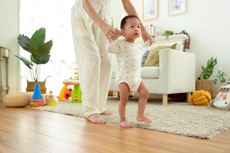 A parent helps a toddler take steps in a warm living room filled with soft light.
