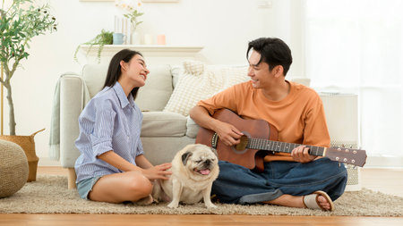Couple is at home sitting on the floor with their dog. One plays a guitar as they relax.