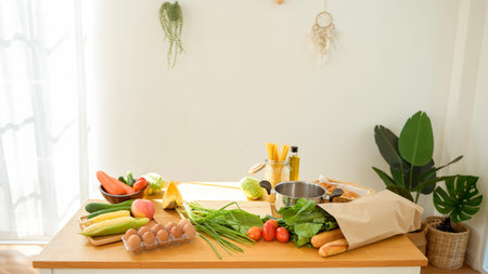 A kitchen table displays fresh vegetables, eggs, and cooking tools for preparing a healthy meal.の写真素材