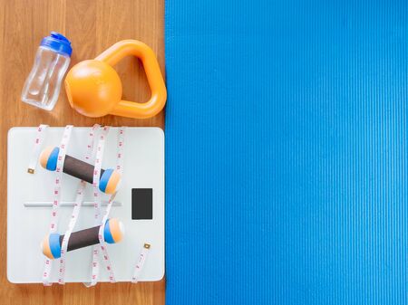 weight loss and physical activity concept from weight scale digital with measure tape for check body shape and workout equipment on a wooden floor.の写真素材