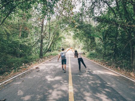 Traveler couple hold hands walking on forest road amid lush trees. Happy couple enjoying free time while traveling.の写真素材