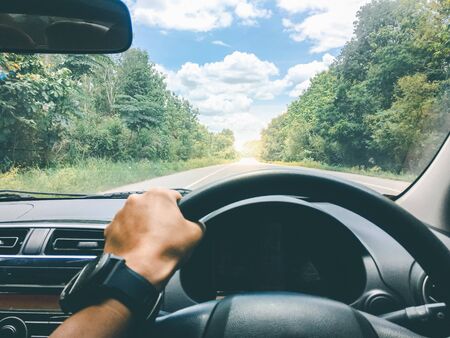 view of driver on the road with green trees against blue sky with clouds.の写真素材
