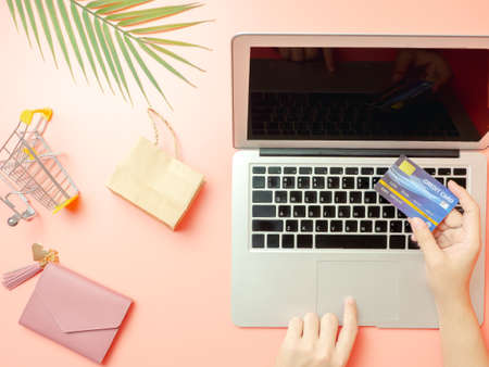 Summer shopping and online payment concept from woman hand holding pink purse with credit card and using laptop for online payment on pastel pink background. Top viewの写真素材