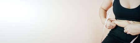 Lose belly fat concept from close up woman in sportswear with hand holding her own belly fat and...