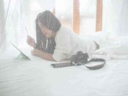 Behind translucent white cloth on bed, Woman working with the tablet at bedroom on the bed after wake up.の写真素材